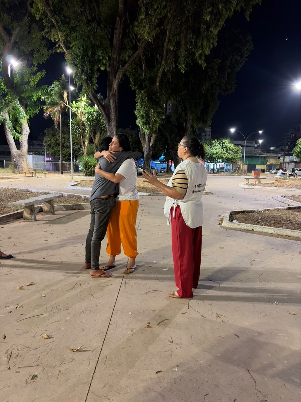 Voluntária abraçando uma pessoa numa praça à noite