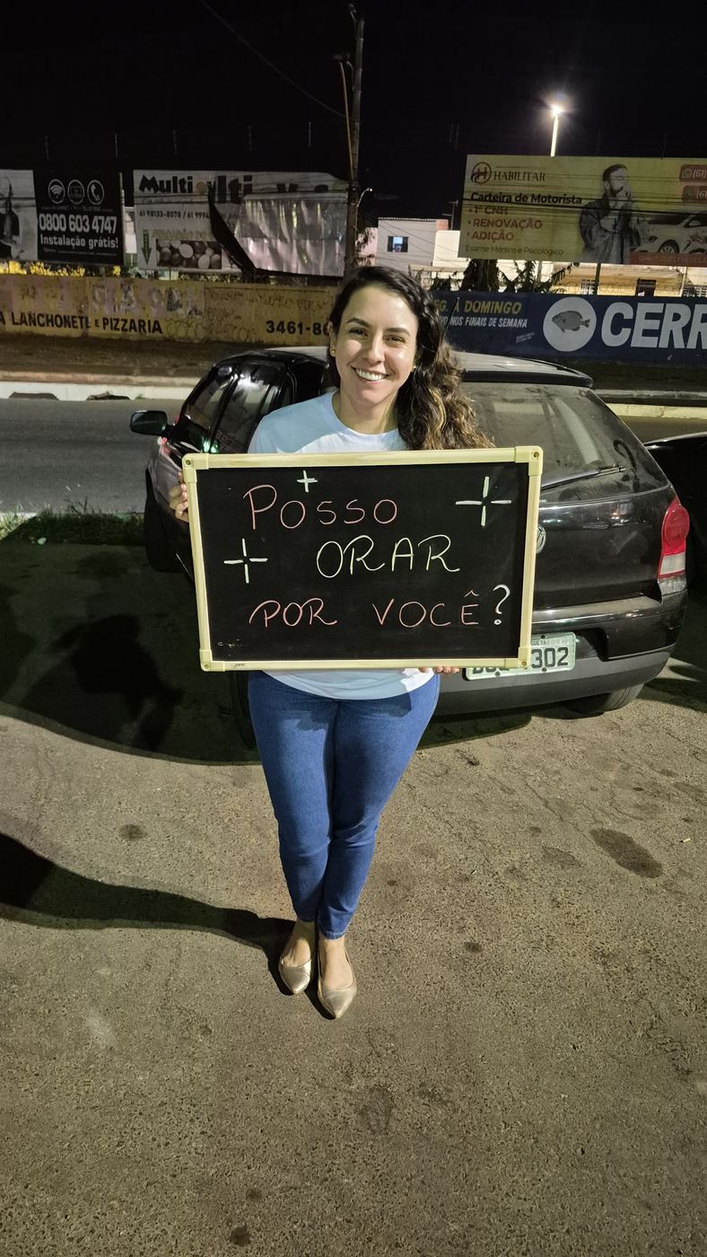 Voluntária segurando uma lousa com a frase Posso orar por você?