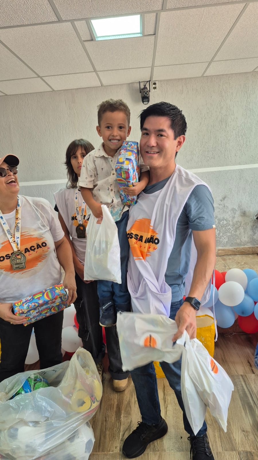 Voluntário da Nossa Ação Diária com um menino sorridente no colo segurando o presente